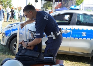 policjant przymierzający dziecku policyjne umundurowanie w tle radiowóz