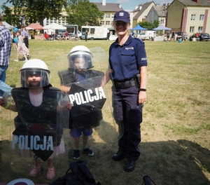 policjantka z dwom chłopcami którzy trzymają tarcze policyjne i mają kaski na głowach