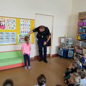 policjant w przedszkolu omawia zasady ruchu drogowego przy tablicy informacyjnej z dziewczynką